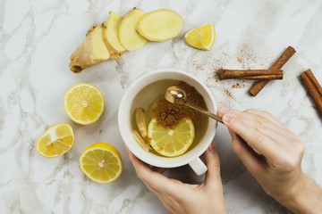 Flatlay of healthy drink with lemon, fresh ginger root, cinnamon sticks and agave syrup on marble...
