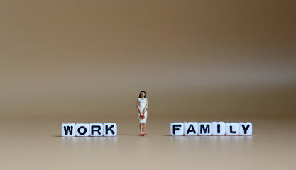A miniature woman standing between a cube of 'WORK' word and a cube of 'FAMILY' word.