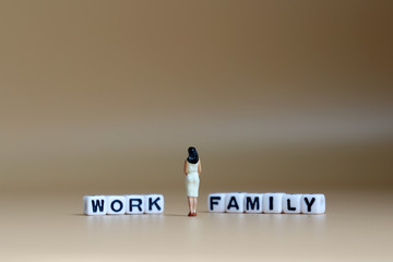 The back of a miniature woman standing between a cube of 'WORK' word and a cube of 'FAMILY' word.
