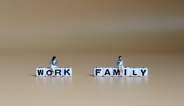 A miniature woman sitting on a cube of 'WORK' word and a miniature woman with baby sitting on a cube of 'FAMILY' word.