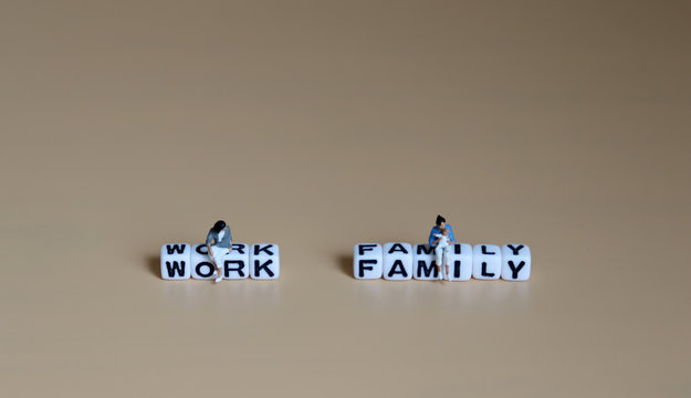 A miniature woman sitting on a cube of 'WORK' word and a miniature woman with baby sitting on a cube of 'FAMILY' word.