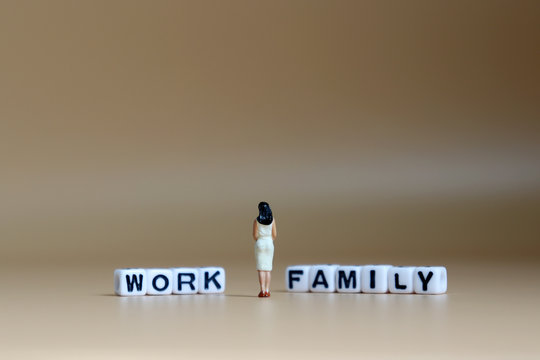 The back of a miniature woman standing between a cube of 'WORK' word and a cube of 'FAMILY' word.