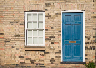 Fototapeta na wymiar Blue vintage front door on a restored brick wall of a Georgian house residential building with white wooden sash window