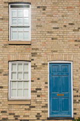 Blue pastel vintage front door on a restored brick wall of a Georgian house residential building with white wooden sash windows
