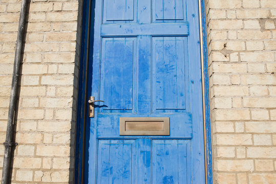 Brass door letterbox on a blue vintage front door on a  yellow brick wall