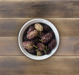 Mulberry fruit. Mulberries in a wooden bowl with copy space for text. Ripe and tasty mulberry on a wooden background. Top view.