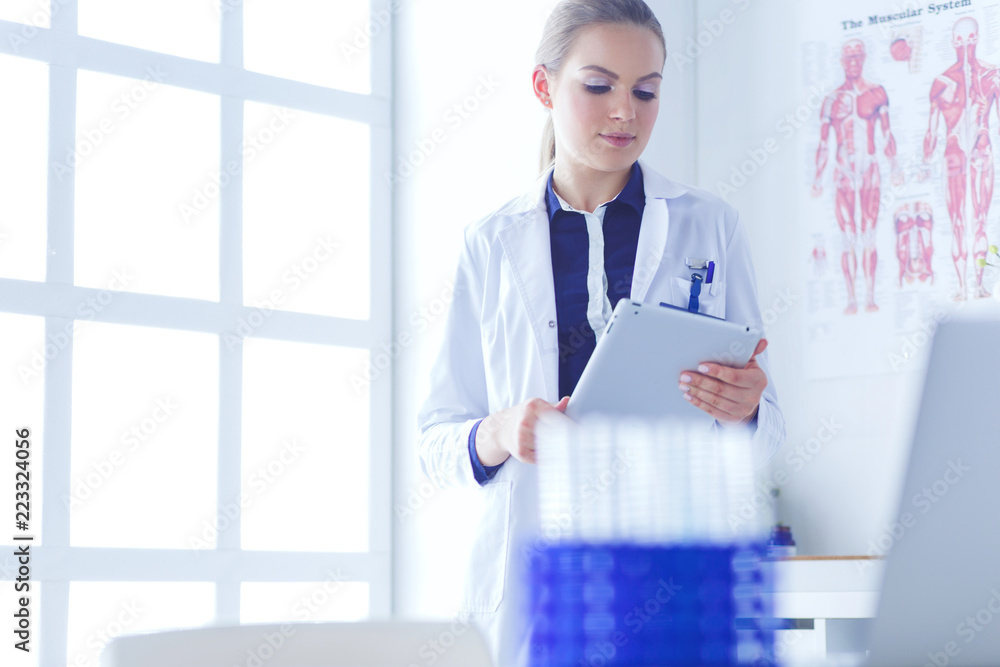 Wall mural Portrait of woman doctor at hospital corridor, holding tablet computer, looking at camera, smiling