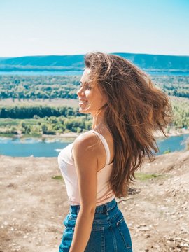A young woman with long hair fluttering in the wind, in a denim skirt posing by the sea overlooking the landscape with water, Islands and forests