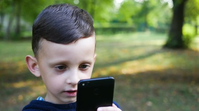 little boy taking photo with his smartphone in the park slow motion