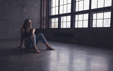 young beautiful woman dancer contemporary in tops and jeans sits on the floor in dance studio