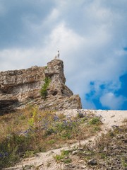 A large stone mountain, on top of which there is a statue of a stone animal, a country road leads to it