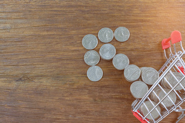 Money and coins in mini shopping cart or trolley on wood background for spending plan, investment, business and finance concept.selective focus.