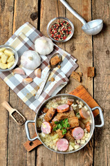 View from above of old saucepan with garlic soup, fresh garlic bulbs, cloves, colored pepper, wooden spoon, croutons, lable and a towel on a rustic wooden table