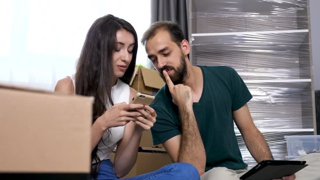 Close up young couple in their new house shopping online for furniture. They are surrounded by cardboard boxes