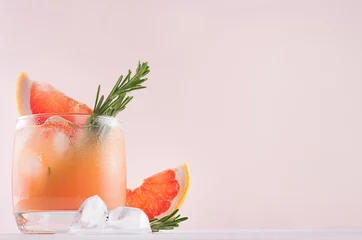 Photo sur Plexiglas Cocktail Cocktail de pamplemousse froid décoré de brindilles de romarin et de tranches d& 39 agrumes en gros plan sur fond rose.