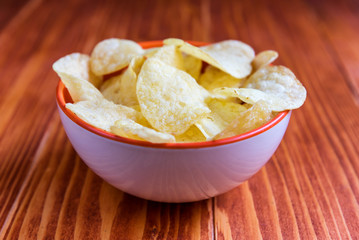 Crispy potato chips in a bowl on wooden background