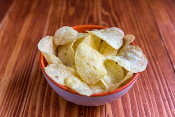 Crispy potato chips in a bowl on wooden background