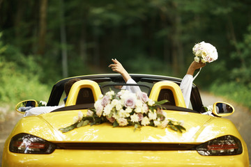 Wedding couple with wedding car. Cabriolet. Back view, bride raised her hands with a bouquet.