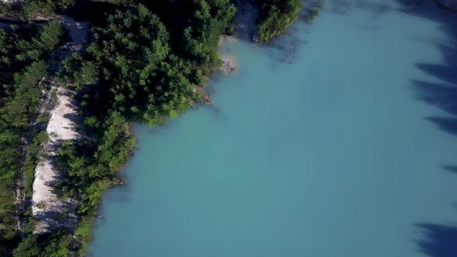 Aerial epic drone flight up from abandoned kaolin quarry with turquoise water, flight with circulating, top down view, sunny evening in anthropogenic landscape of South Ural, Russia