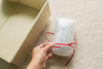 close up woman tie a red ribbon on gift wrapped with bubble sheet before putting into carton for parcel