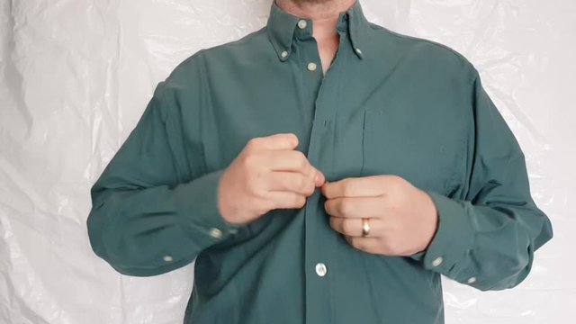 Male with a partially amputated index finger on his right hand stood buttoning up a green shirt.