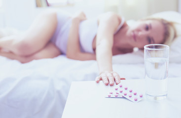 Young beautiful woman with pills lying on bed in bedroom
