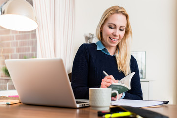 Portrait of a smiling woman at her desk writing on book