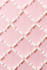 Pattern of white pills and tablets on a pink background.