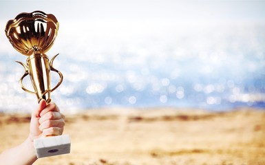 Hand holding golden trophy on beach background