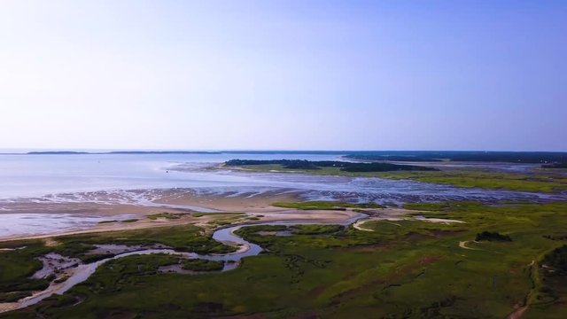 Sunken Meadows on Cape Cod, MA. The marsh and channels of water connect to the bay. The tide is low and much of the beach is freshly exposed. The camera pans to the left as it ascends.