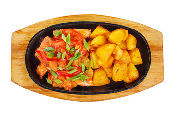 Potatoes with meat, pork, chicken, bell pepper and green onion, with sweet and sour sauce, fried, baked portion on a hot frying pan, on a wooden board on white background view from above. For the menu