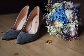 Fototapeta na wymiar gray shoes, wedding rings and a bouquet of the bride on a wooden table