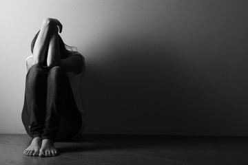 Teenager girl with depression sitting alone on the floor in the dark room.  Black and white photo - obrazy, fototapety, plakaty