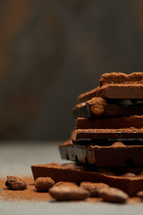 close-up view of stacked delicious assorted chocolate pieces with nuts and cocoa beans on grey