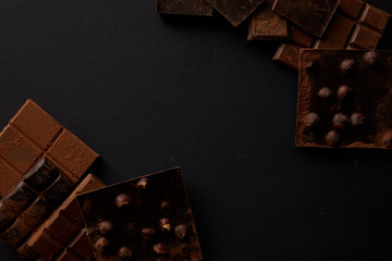 top view of assorted delicious chocolate pieces with hazelnuts on black background