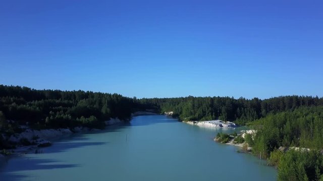 Aerial epic drone flight to the abandoned kaolin quarry over the turquoise water through the branches pine tree, flight to the horizon, sunny evening in anthropogenic landscape of South Ural, Russia