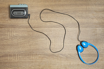 Retro black walkman and blue headphones on wooden background.
