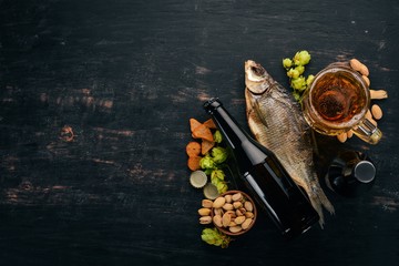 Beer and snacks. Salted crackers, Dried Fish, Chips, Nuts, Peanuts, Pistachios. On a black wooden background. Free space for text. Top view.