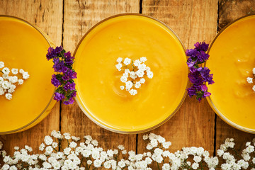 fresh and delicious pumpkin soup and flowers on an old wooden kitchen table