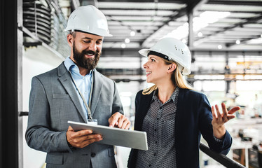 A portrait of an industrial man and woman engineer with tablet in a factory, working.