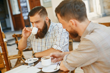 two men drink coffee at a cafe