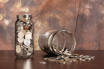 Money in jars and pile of coins scattered on table
