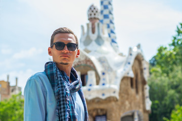 A young guy stands in a sunglasses near a gingerbread house in Guell Park in Barcelona, Spain
