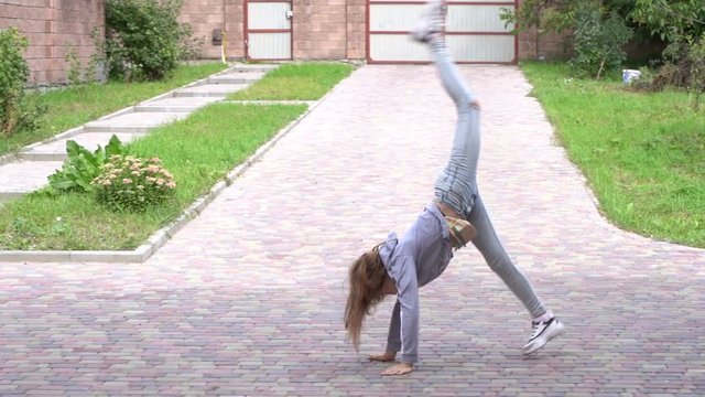 Young flexible girl does cartwheel across frame, outdoors, slow motion. Teenager girl doing acrobatic stunt in yard