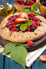 Whole-grain galette with plums and berries on dark background, top view