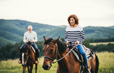 A senior couple riding horses in nature.