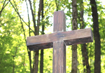 Wooden Christian religious cross on the background of green trees and rays of sunlight at dawn
