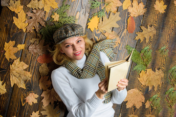 She likes detective genre. Girl blonde lay wooden background with leaves. Woman lady in checkered...