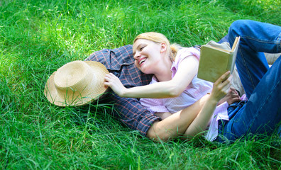 Man and girl lay on green grass having fun. Couple in love spend leisure reading book. Couple...