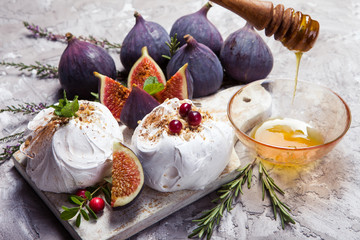 Delicious mini pavlova cake with figs, cranberries, mint leaves and sweet honey on concrete background